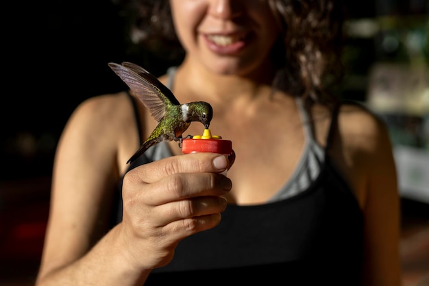 Mujer latinoamericana sostiene un alimentador de colibríes en sus manos mientras se alimenta de comida