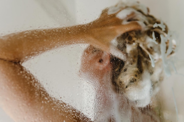 La mujer se lava el pelo con champú mientras se ducha