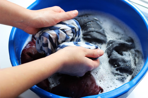 Una mujer lava la ropa con las manos en agua con jabón.