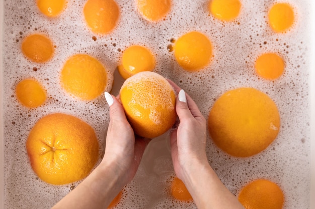 Mujer lavando naranja madura, pomelo debajo del grifo en la cocina del fregadero, remojando las frutas en agua jabonosa lava a fondo después de la tienda.