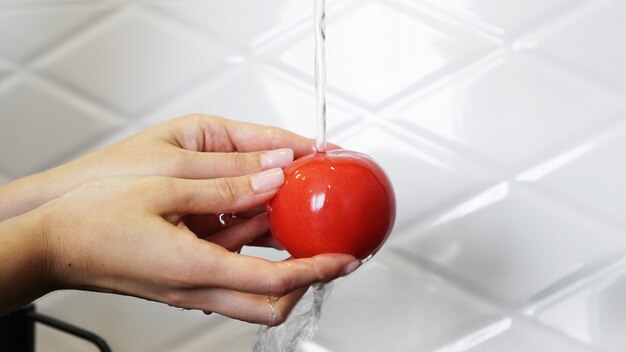 Mujer lavando tomates y tomate en sus manos - fondo blanco de la cocina