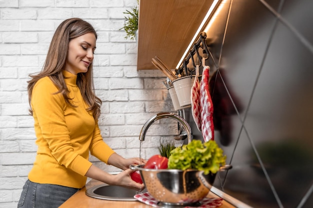 Mujer lavando verduras en la cocina de casa