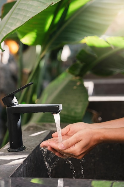 Mujer lavándose las manos con agua de grifo en un fregadero de piedra en un baño al aire libre con hojas tropicales