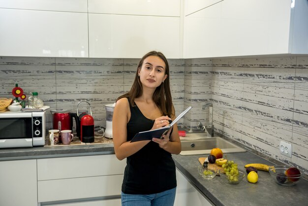 mujer lee un cuaderno en la cocina para cocinar alimentos saludables