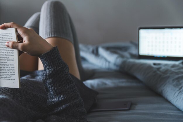 Mujer lee el libro en la cama. portátil en el fondo. estudiar en la cama