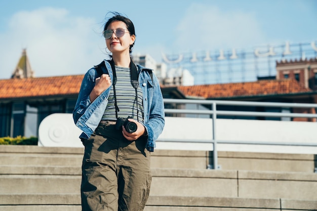 mujer lente hombre sosteniendo la cámara bajando las escaleras. joven estudiante con gafas de sol haciendo turismo en el muelle 39 de san francisco. dama viajera viaje autoguiado en américa en vacaciones de verano.