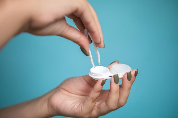 Mujer con lentes de contacto y pinzas sobre fondo azul, primer plano