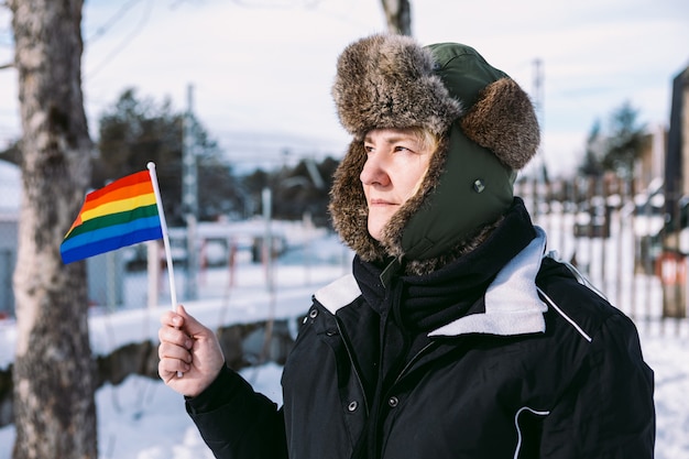 Mujer lesbiana con un gorro de nieve para el cabello, en una zona nevada sosteniendo la bandera del arco iris lgbt