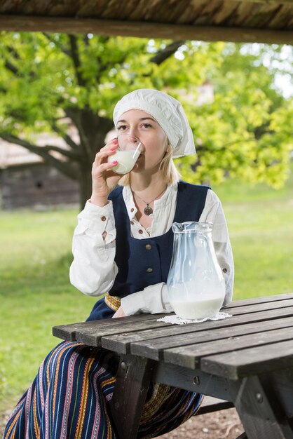 Mujer letona en ropa tradicional con vaso de leche en la naturaleza