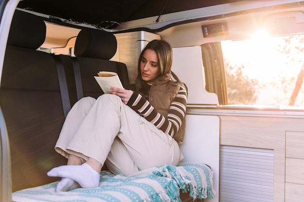 Mujer leyendo un libro en una acogedora autocaravana al atardecer