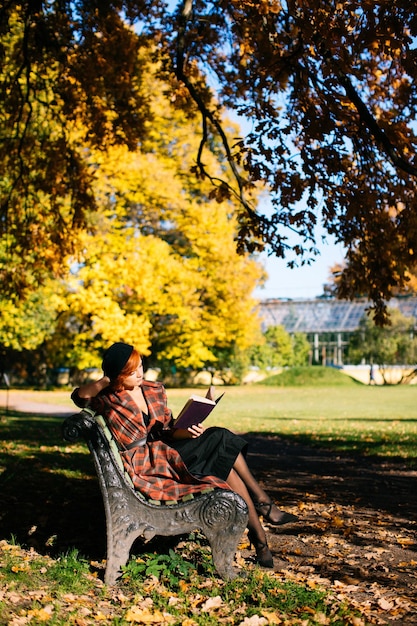 Foto mujer leyendo un libro en un banco en un parque de otoño en un día soleado estado de ánimo de otoño tiempo de relajación en el parque de la ciudad