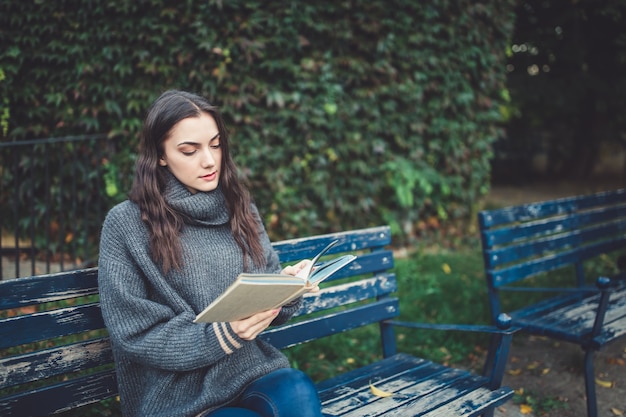 Mujer leyendo un libro en el banco de un parque