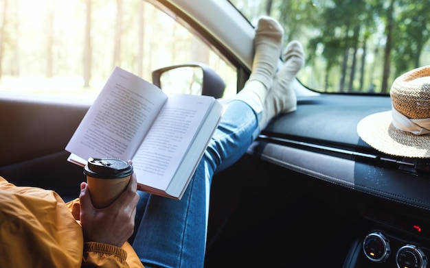 Una mujer leyendo un libro y bebiendo café en el auto.