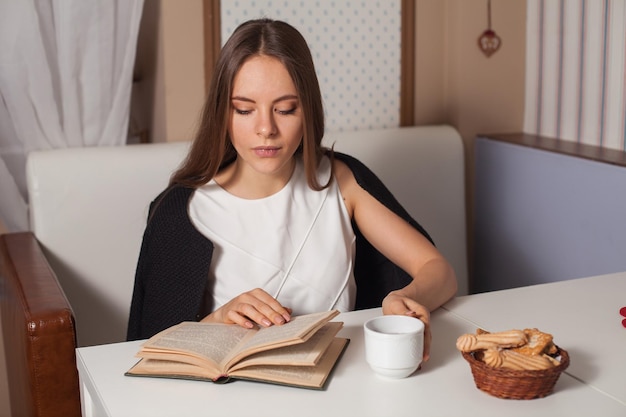 Mujer leyendo un libro en la cafetería y bebiendo té