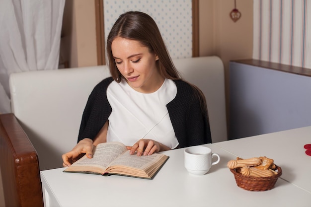 Mujer leyendo un libro en la cafetería y bebiendo té