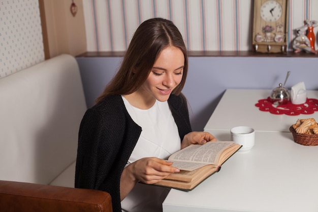 Mujer leyendo un libro en la cafetería y bebiendo té