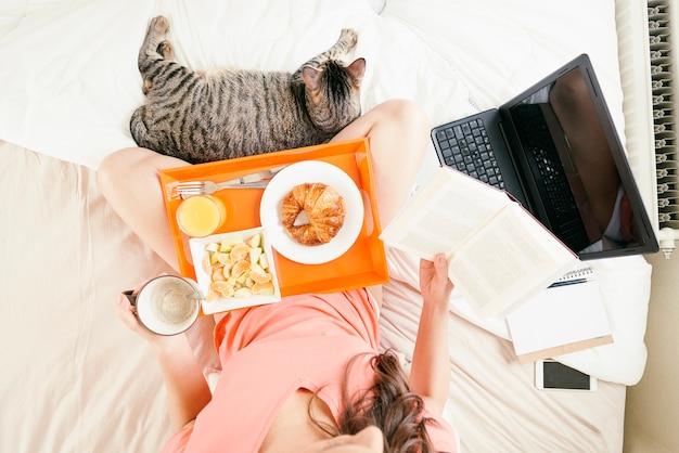 Foto mujer leyendo el libro y desayunando. ella está en su dormitorio. vista aérea