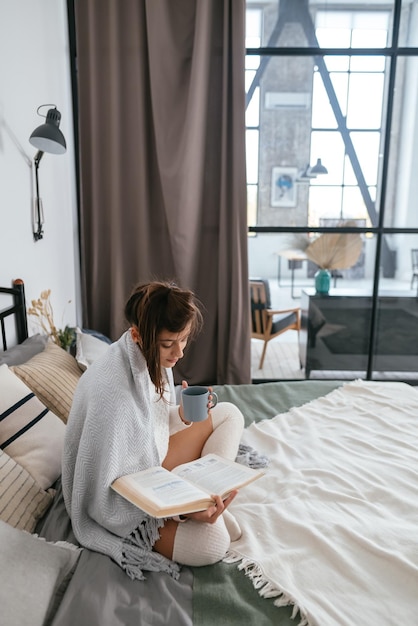 Mujer leyendo un libro y disfrutando de un café caliente en un apartamento soleado