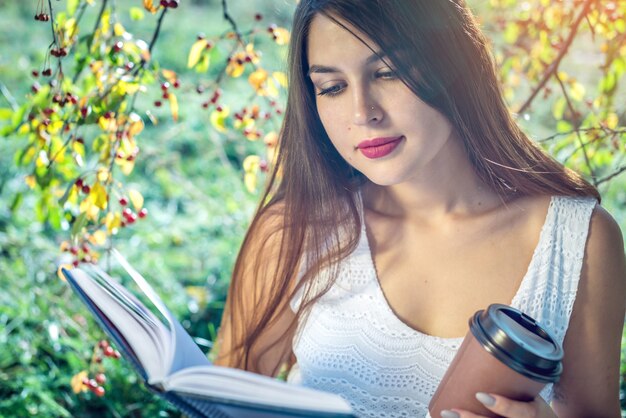 Foto mujer leyendo un libro interesante sentado en un parque en un césped verde