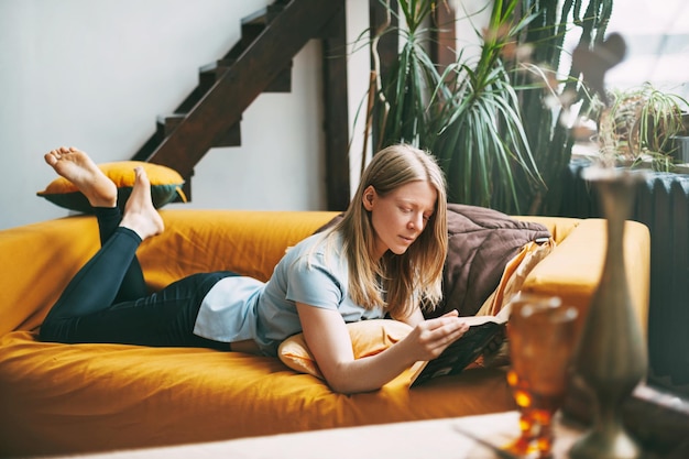 Foto mujer leyendo un libro mientras está acostada en el sofá en casa