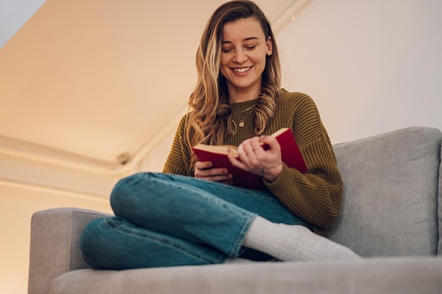 Mujer leyendo un libro mientras está sentada en el sofá en casa