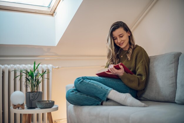 Mujer leyendo un libro mientras está sentada en el sofá en casa