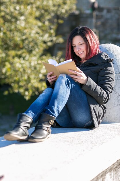 Foto mujer leyendo un libro mientras está sentada en la barandilla