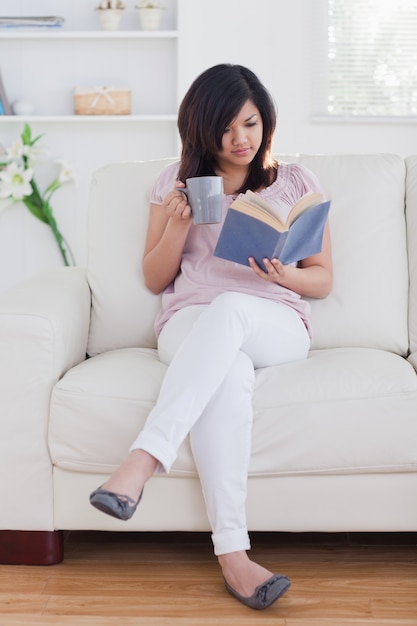 Mujer leyendo un libro mientras sostiene una taza