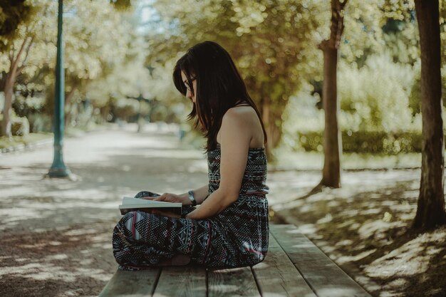 Foto mujer leyendo un libro sentada en un banco en el parque