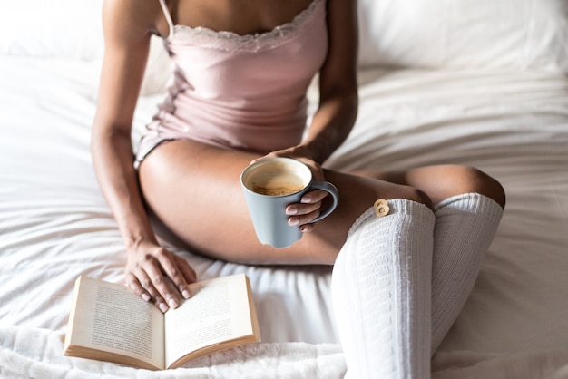 Mujer leyendo un libro y tomando café en la cama con calcetines