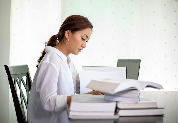 mujer leyendo un libro y usando el cuaderno trabajando desde casa