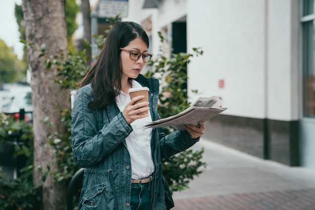 mujer leyendo un periódico mientras bebe una taza de café y lista para su trabajo de oficina.