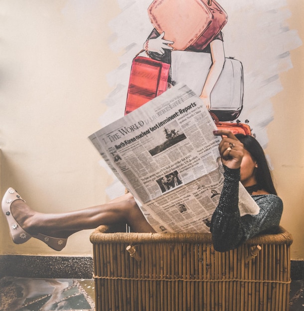 Foto mujer leyendo el periódico mientras está sentada en la canasta en casa