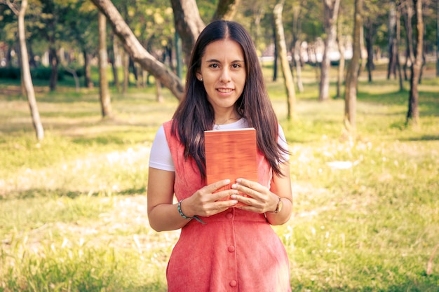 Mujer con un libro caminando en el parque con árboles en el fondo