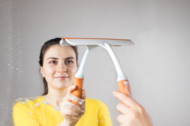 Una mujer limpia el espejo con un dispensador de agua y limpiacristales.