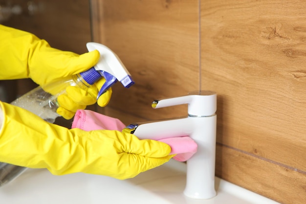 La mujer limpia el fregadero y el grifo en la limpieza y desinfección del baño.