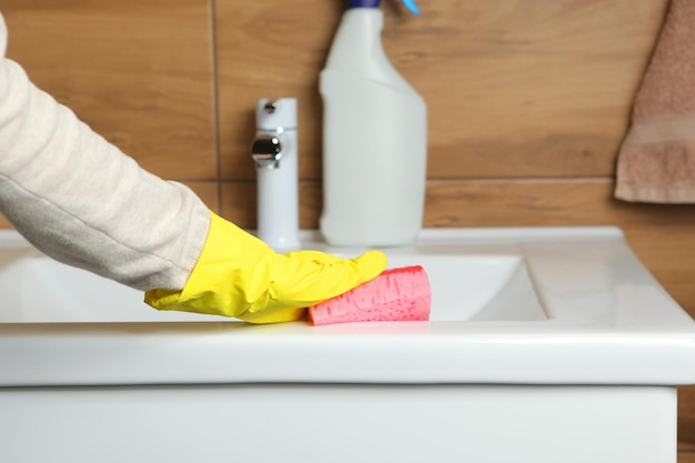 La mujer limpia el fregadero y el grifo en la limpieza y desinfección del baño.