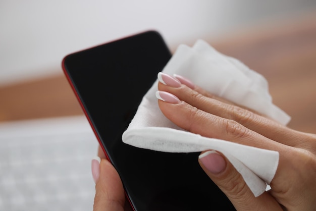 Mujer limpia la pantalla del teléfono móvil con un paño húmedo antibacteriano y procedimiento de desinfección