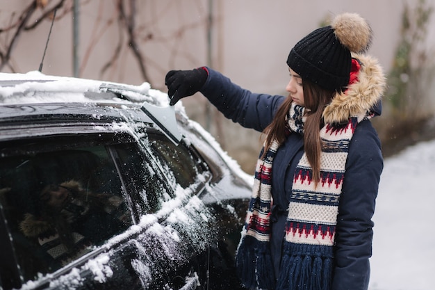 Una mujer limpia la ventana nevada de un automóvil con un raspador de nieve.