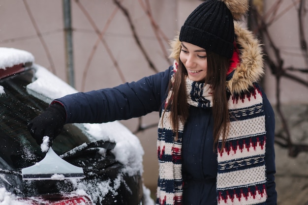 Una mujer limpia la ventana nevada de un automóvil con un raspador de nieve.