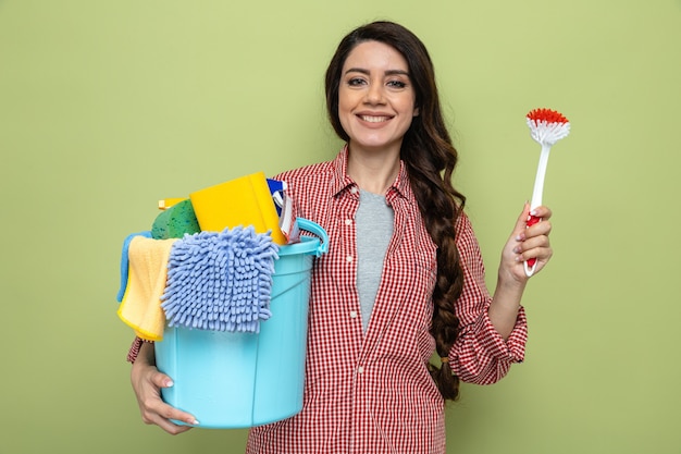 Mujer limpiador bastante caucásica sonriente que sostiene el cepillo y el equipo de limpieza