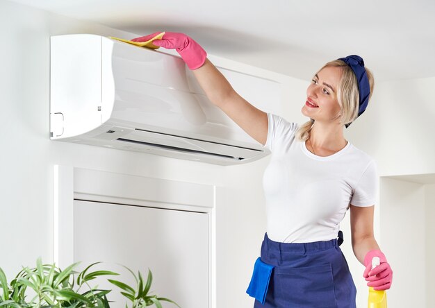 Mujer limpiando el aire acondicionado con un trapo. Servicio de limpieza o concepto de ama de casa