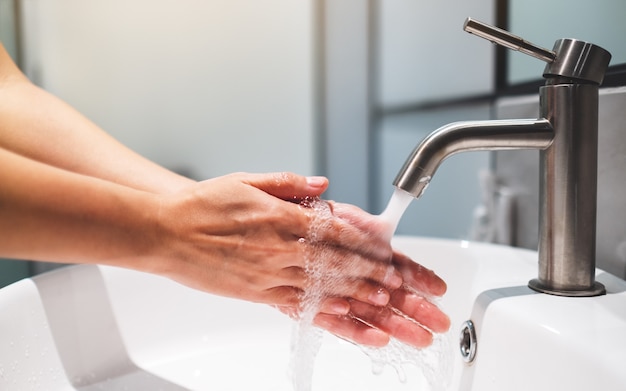 Mujer limpiando y lavándose las manos debajo del grifo del baño