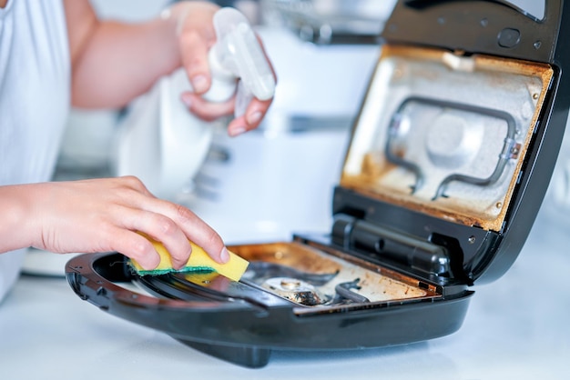 Mujer limpiando parrilla o tostadora en la cocina