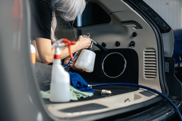 Mujer limpiando salón de autos con spray pulidor en servicio de detallado de autos