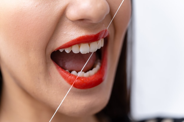 Mujer limpiando sus dientes con hilo dental. Primer plano, foto recortada.