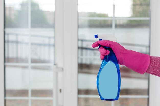 Foto mujer limpiando una ventana con rociador de limpieza.