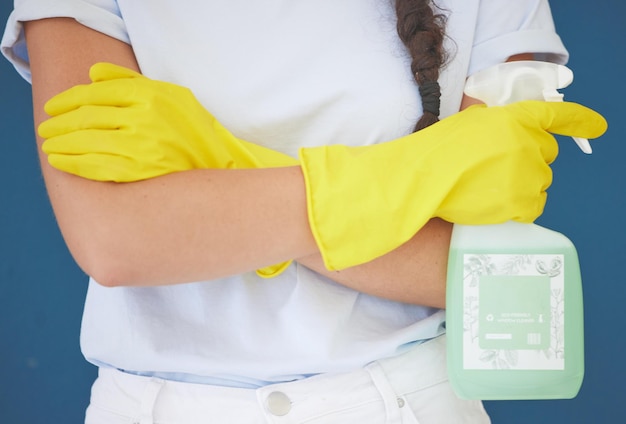 Mujer de limpieza y brazos cruzados con producto en aerosol para la rutina de higiene y saneamiento del hogar en estudio azul Chica de limpieza con botella de detergente químico y guantes de seguridad para limpieza de primavera