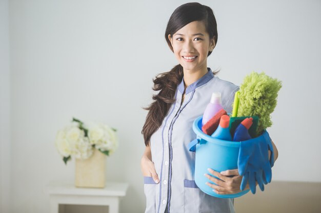 Mujer de limpieza mucama sonriendo y sosteniendo un cubo con productos de limpieza