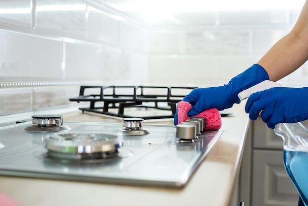 Mujer limpieza de superficie de gas de acero inoxidable en la cocina con guantes de goma.